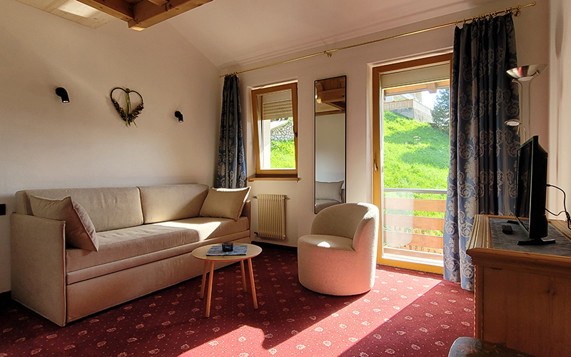 Spacious suite at Garni Royal in Arabba with sofa bed, armchair, TV, and balcony with Dolomites view.