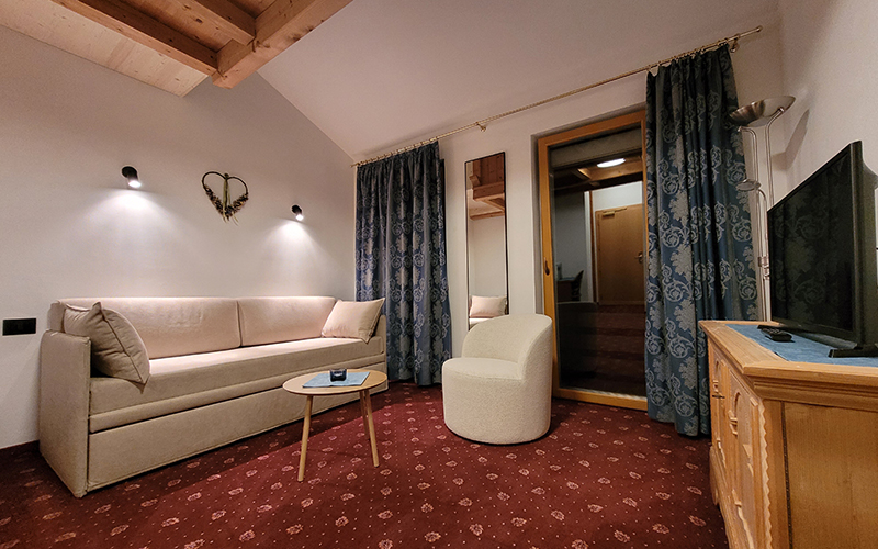 Spacious suite at Garni Royal in Arabba with a sofa bed, armchair, red carpet, and balcony access.