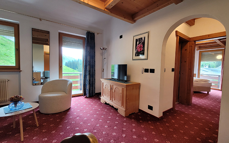 Spacious suite at Garni Royal in Arabba with red carpet, balcony with Dolomite view, and wooden furnishings.