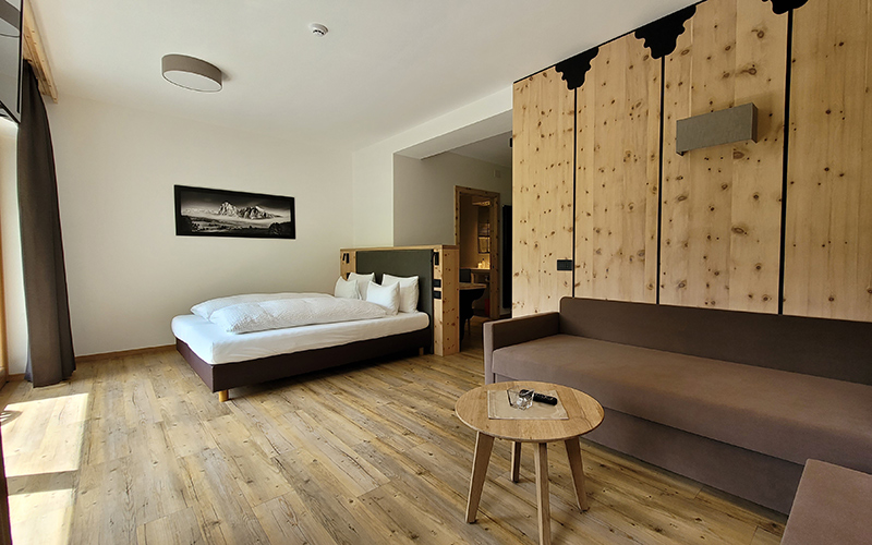 Garni Royal suite in Arabba with a double bed, sofa, wooden floor, and Swiss pine wall.