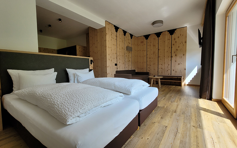 Double room at Garni Royal in Arabba with separate beds, wooden floor, and pine wood wall.