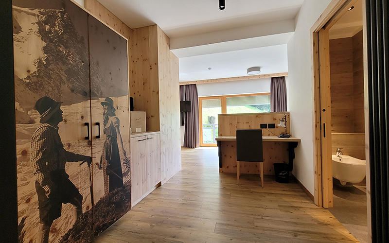 Spacious Swiss pine wood suite at Garni Royal in Arabba, with a double bed, desk, and balcony with Dolomite views.