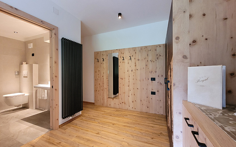 Stone pine wood corridor with mirror, coat rack, and access to a modern bathroom, typical of the rooms at Garni Royal in Arabba.