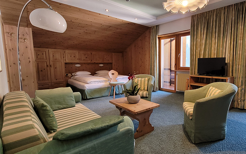 Stone pine wood suite at Garni Royal in Arabba with single beds, sofa, armchairs, and balcony.