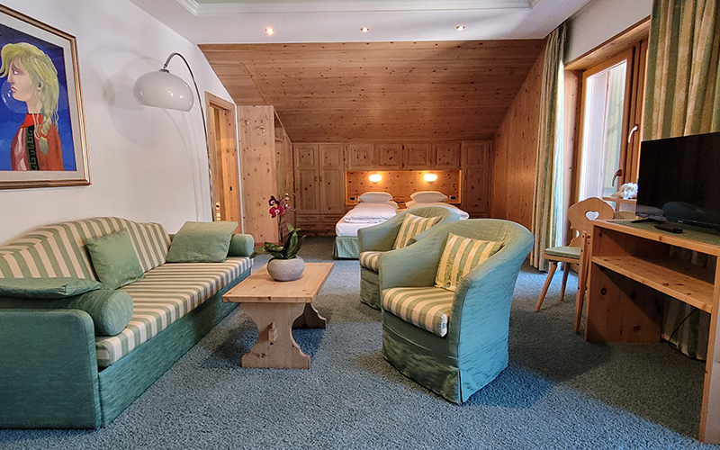 Garni Royal suite in Arabba with sofa, armchairs, single beds, and Swiss pine wood furnishings.
