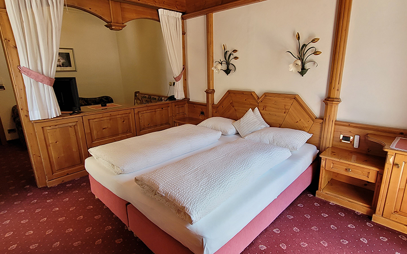 Double room at Garni Royal in Arabba, with a king-size bed, Swiss pine wood furnishings, and a red carpet.