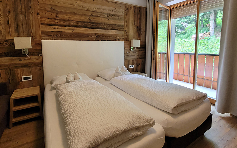 Double room at Garni Royal in Arabba, with Swiss pine wood walls, single beds, and a balcony with a view of the Dolomites.