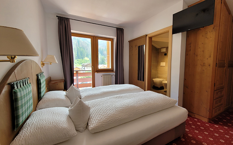 Alpenroyal apartment in Arabba: living room with sofa bed, dining table, and view of the Dolomites.