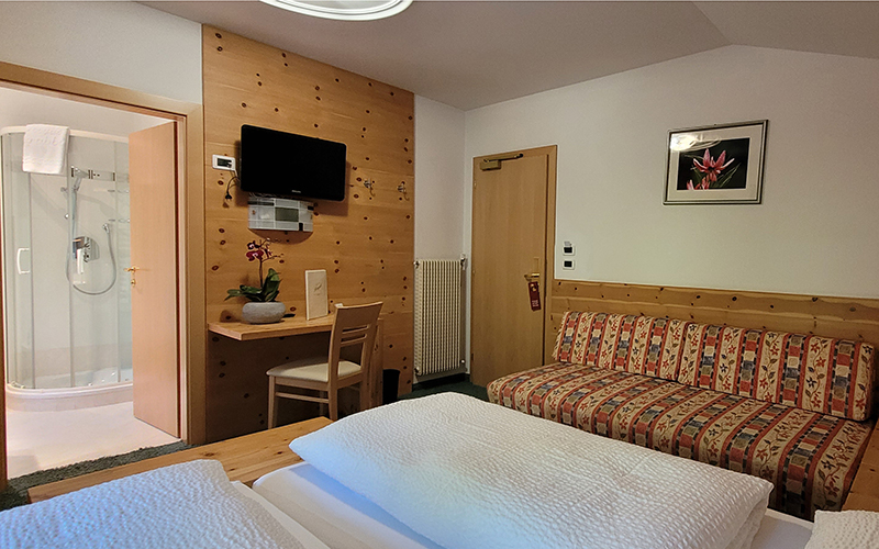 Light wooden double bedroom with exposed beams, bed with white sheets, and a nightstand.