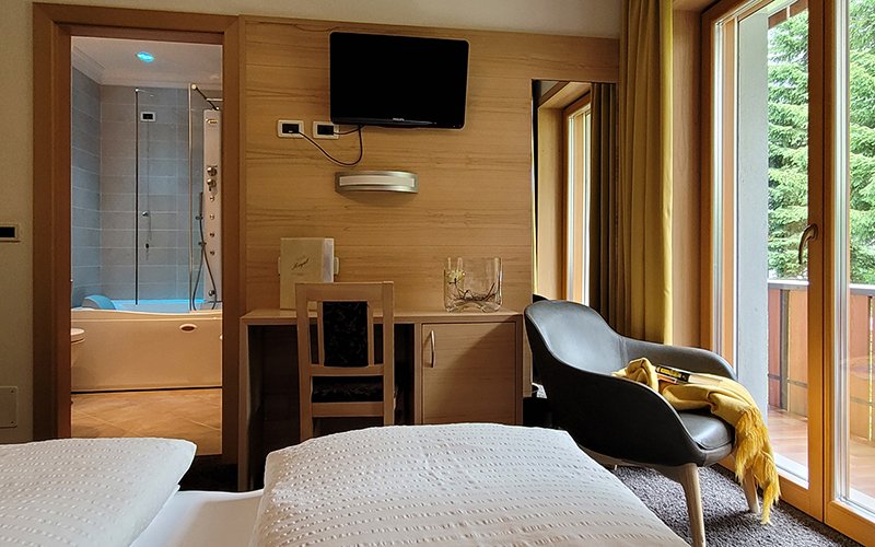 Stone pine wood suite at Garni Royal in Arabba with bed, desk, armchair, TV, and bathroom with whirlpool tub.