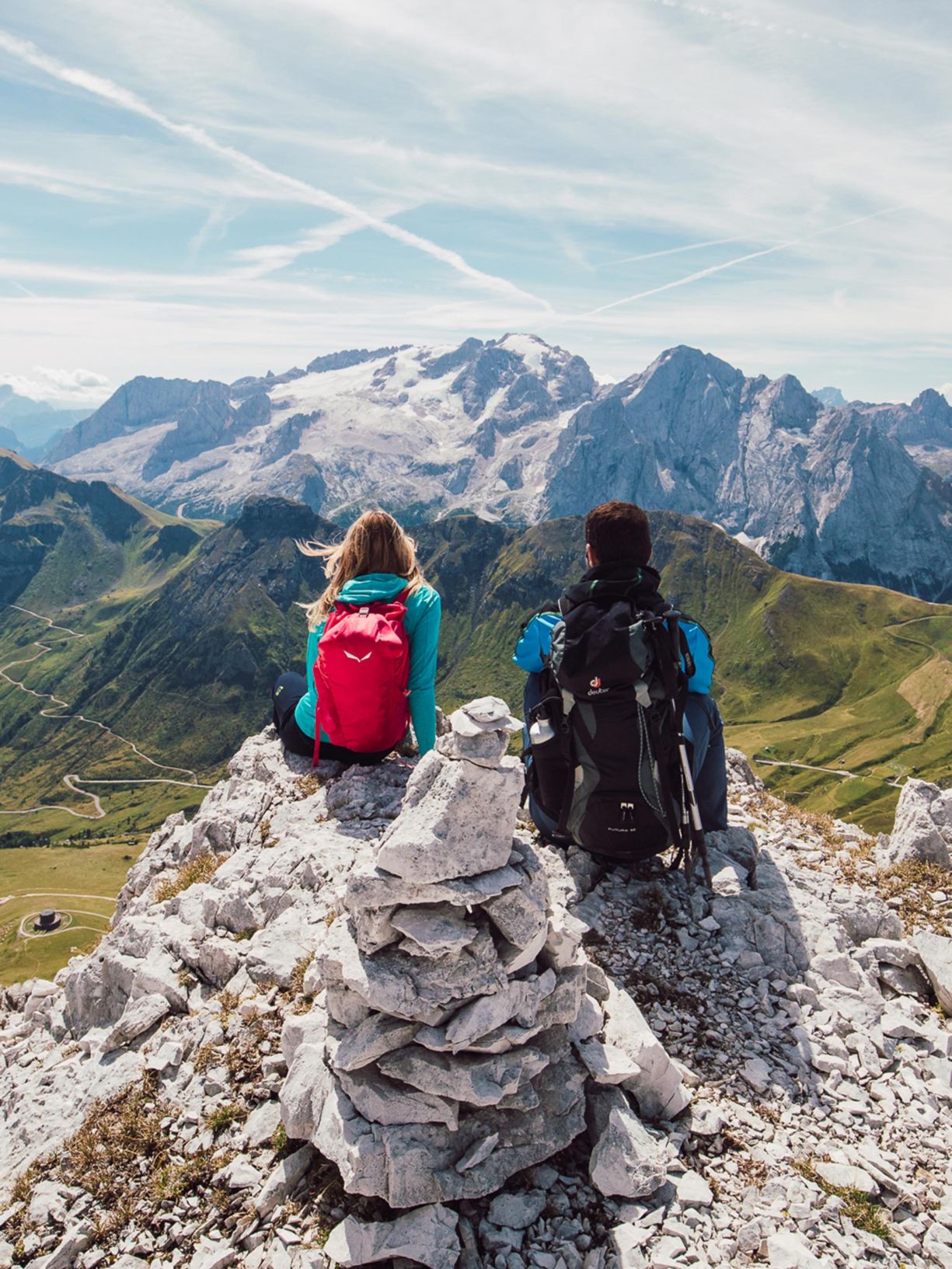 Due escursionisti con zaini ammirano le Dolomiti innevate da una cima rocciosa ad Arabba.
