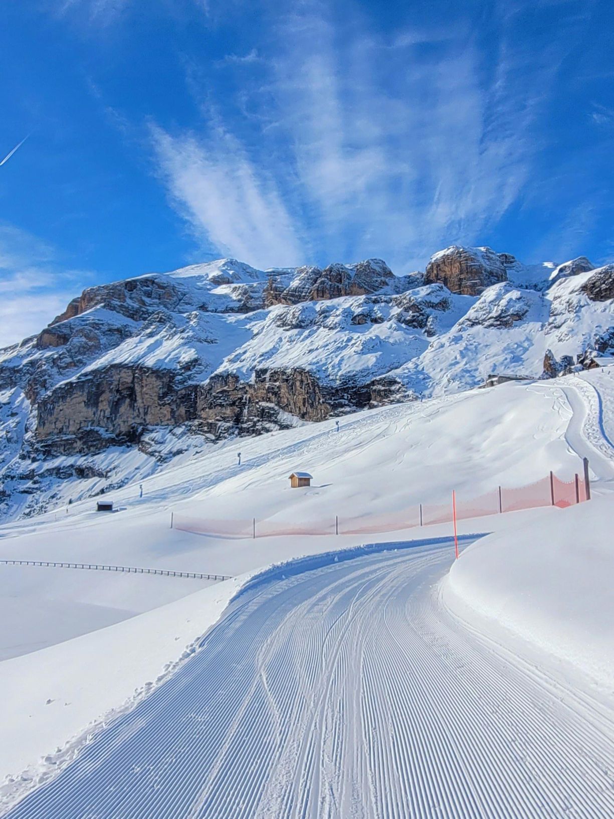 Una pista da sci perfettamente battuta ad Arabba, con le maestose Dolomiti innevate e un cielo azzurro.