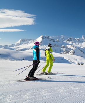 Due sciatori con abbigliamento colorato ammirano le Dolomiti innevate di Arabba, perfette per una vacanza sciistica.
