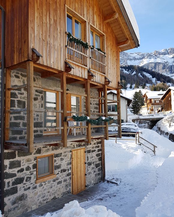 Lo Chalet Royal ad Arabba, con balconi in legno e pareti in pietra, immerso nella neve delle Dolomiti.